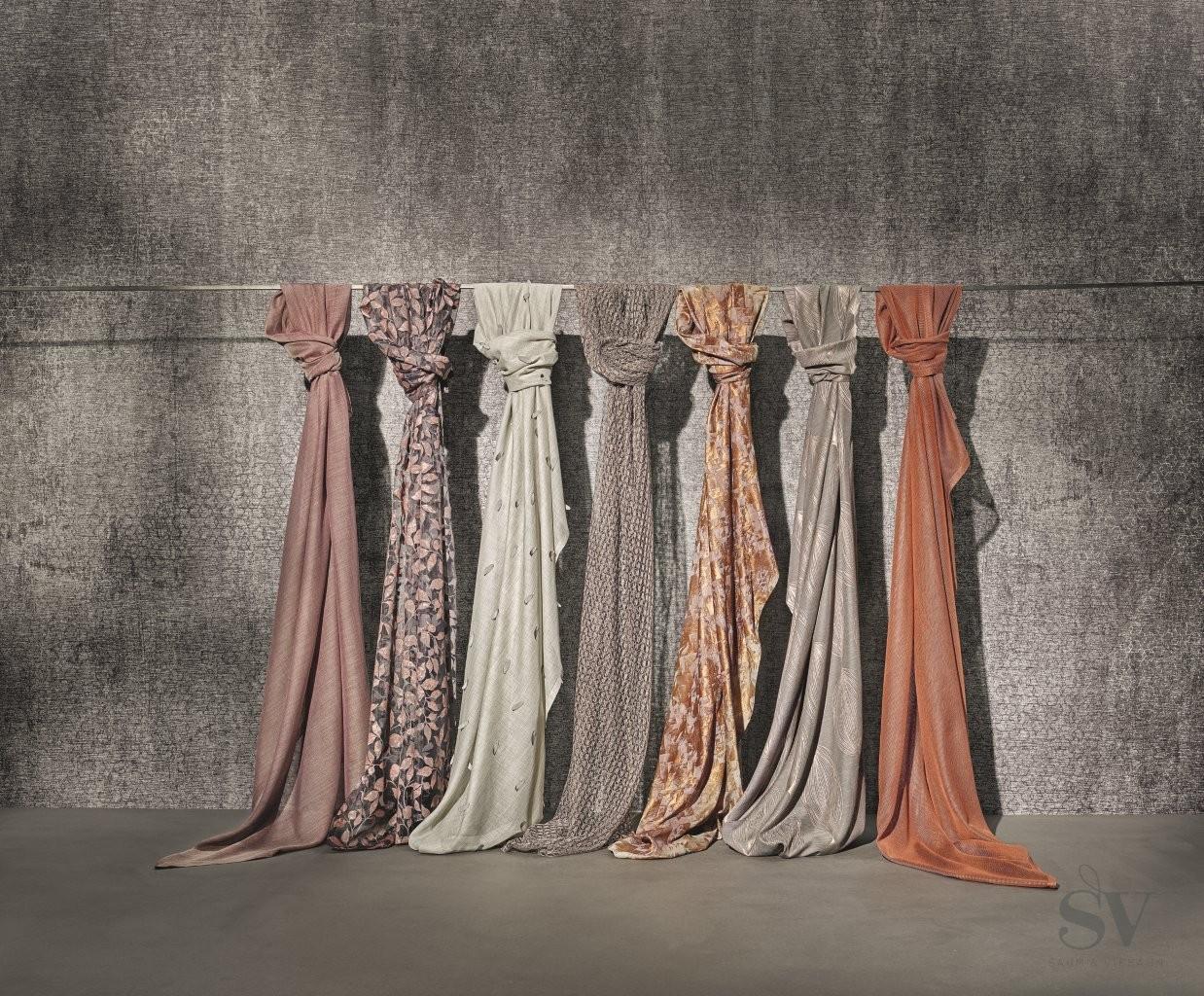 Mehrere lang fallende Stoffbahnen, gebunden an einer Stange vor einer Betonwand